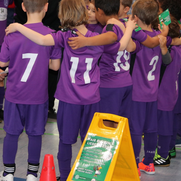 Bambini Spieler in Lila Trikots von hinten. Sie stehen im Kreis und haben die Arme umeinander gelegt.