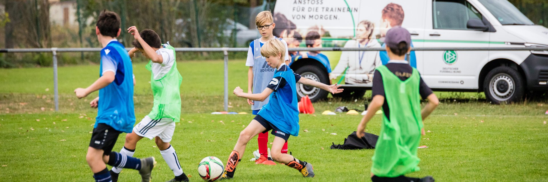 Eine Gruppe Kinder, die Fußball spielen. Im Hintergrund steht das DFB-Mobil mit einem offenen Kofferraum.