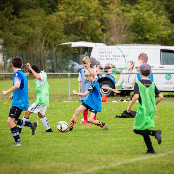 Eine Gruppe Kinder, die Fußball spielen. Im Hintergrund steht das DFB-Mobil mit einem offenen Kofferraum.