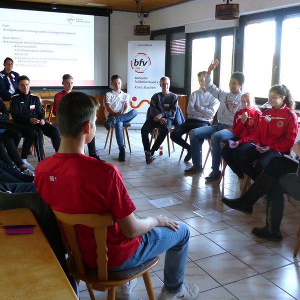 Auf diesem Bild ist ein Führungsspielertreff zu sehen. Viele Jugendliche sitzen in einem Stuhlkreis und unterhalten sich.