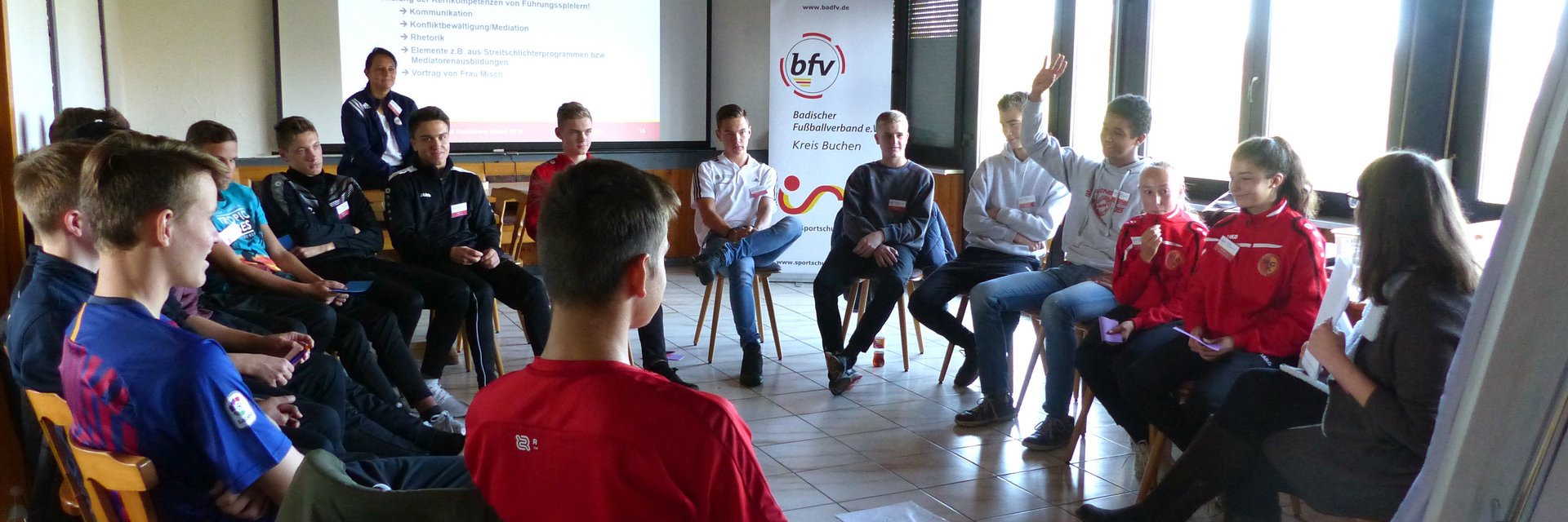 Auf diesem Bild ist ein Führungsspielertreff zu sehen. Viele Jugendliche sitzen in einem Stuhlkreis und unterhalten sich.