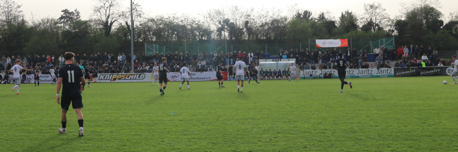 Eine Spielsituation. Zwei Jugendmannschaften spielen gegeneinander, im Hintergrund ist die Tribüne mit Zuschauern gefüllt.