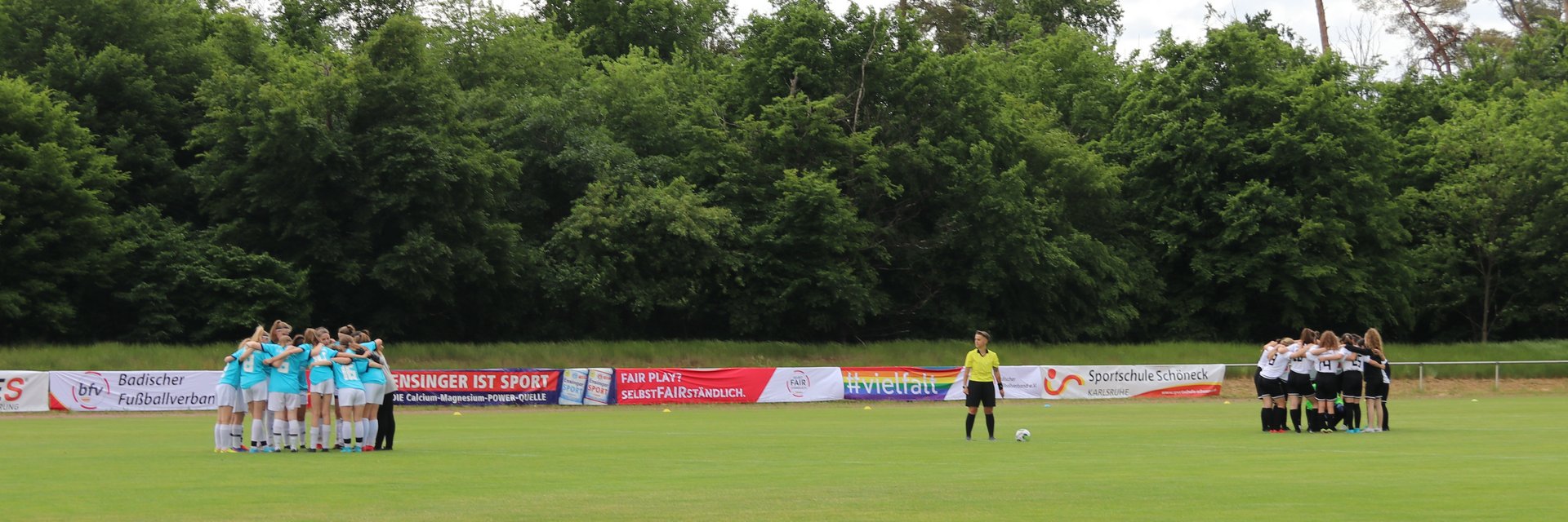 Zwei Juniorinnenmannschaften, die vor dem Anpfiff in ihrer jeweiligen Hälfte des Platzes in einem Kreis stehen