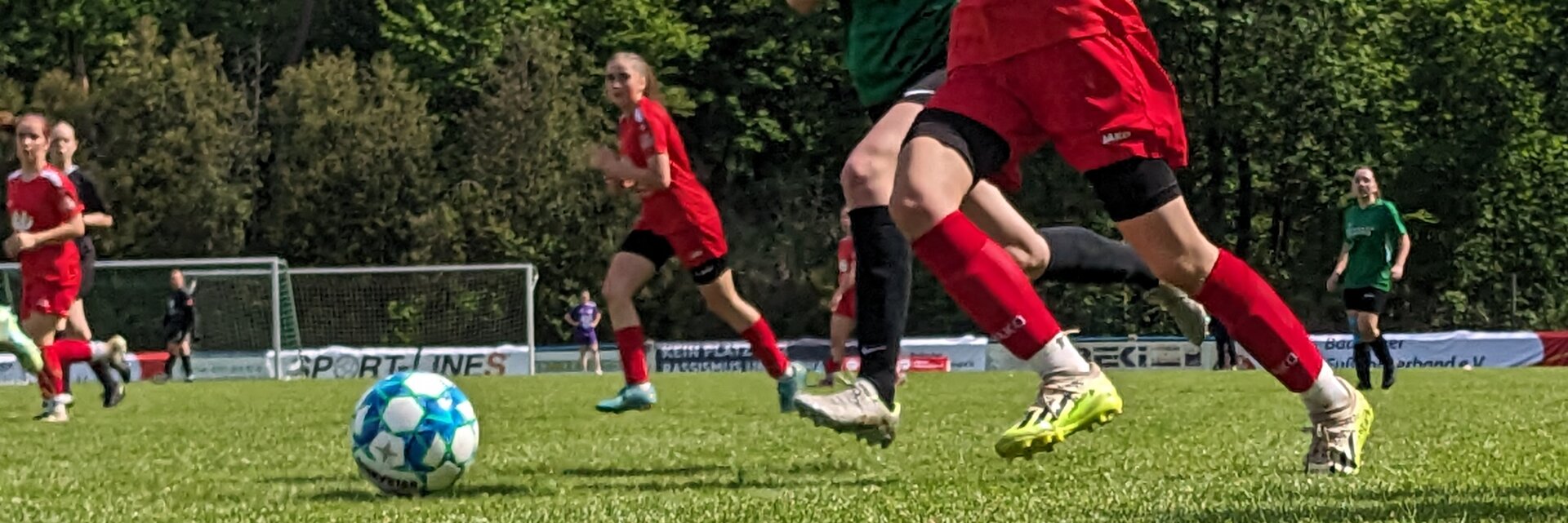 Zwei Spielerinnen, die einen Zweikampf führen. Eine von ihnen trägt ein grünes Trikot, die andere ein rotes.