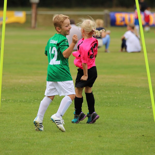 Ein Junge in einem grünen Trikot und ein Mädchen in einem rosa Trikot, die auf einem Fußballplatz zusammen spielen.