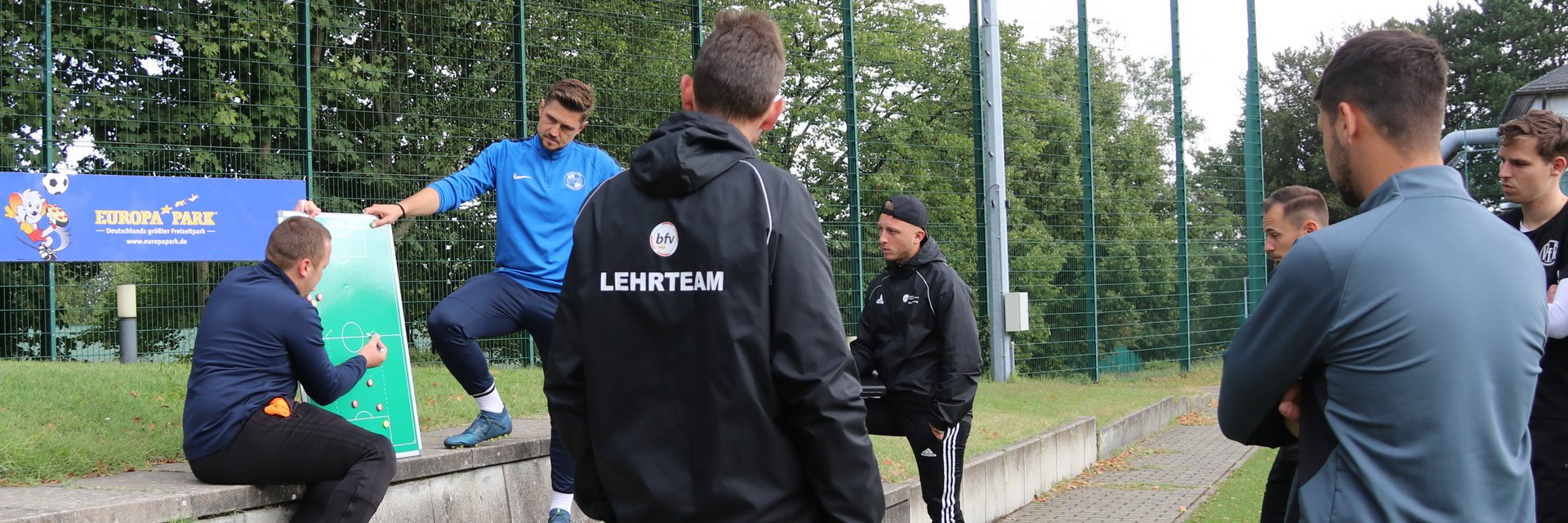 Eine Szene aus einem B-Lizenz Lehrgang. Zwei Teilnehmer erklären etwas an der Taktiktafel, der Rest hört ihnen zu.