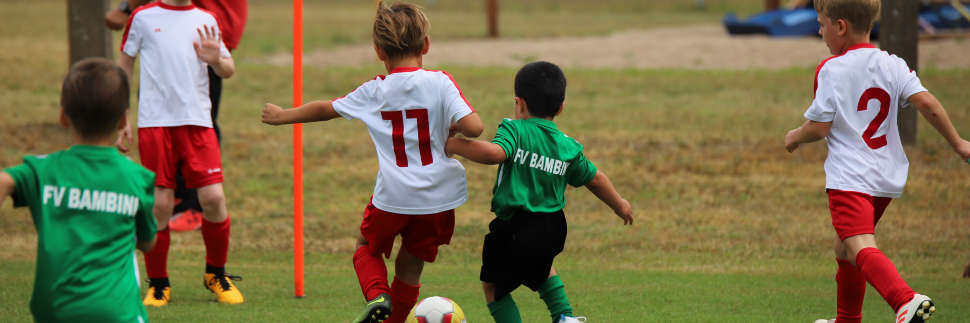 Fünf Jungen von zwei Mannschaften, die gegeneinander Fußball spielen. In der Bildmitte führen zwei von ihnen gerade einen Zweikampf um den Ball.
