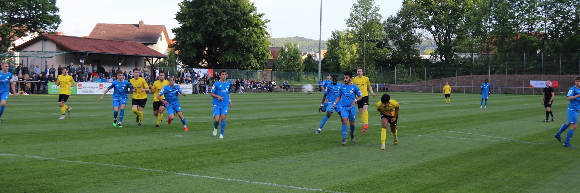 Eine Spielsituation aus einem Juniorenspiel. Eine Mannschaft in blau und eine in gelb spielen gegeneinander. Der Ball wurde von einem Spieler nach außen weggeschossen.