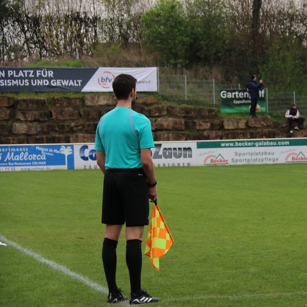 Linienrichter von hinten, er steht am Spielfeldrand und hält eine Fahne in der Hand