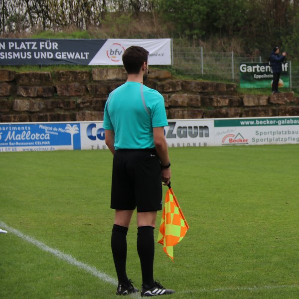 Linienrichter von hinten, er steht am Spielfeldrand und hält eine Fahne in der Hand