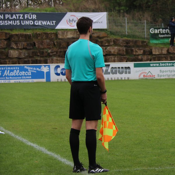 Linienrichter von hinten, er steht am Spielfeldrand und hält eine Fahne in der Hand