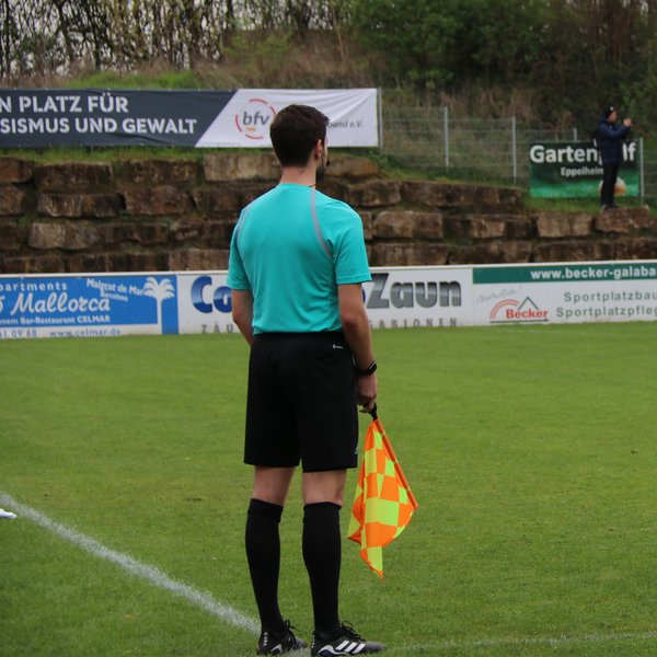 Linienrichter von hinten, er steht am Spielfeldrand und hält eine Fahne in der Hand