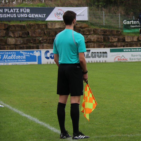 Linienrichter von hinten, er steht am Spielfeldrand und hält eine Fahne in der Hand