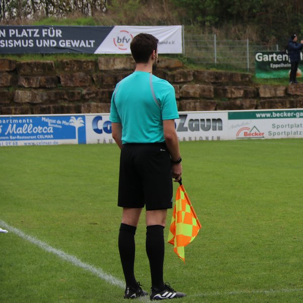 Linienrichter von hinten, er steht am Spielfeldrand und hält eine Fahne in der Hand