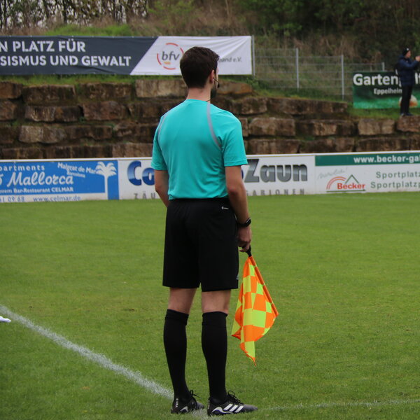 Linienrichter von hinten, er steht am Spielfeldrand und hält eine Fahne in der Hand