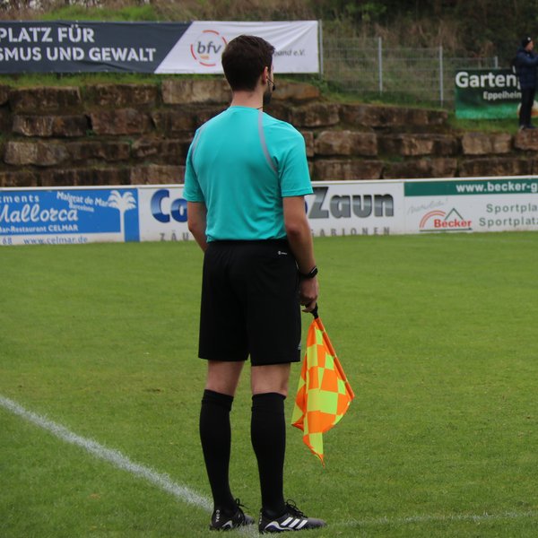 Linienrichter von hinten, er steht am Spielfeldrand und hält eine Fahne in der Hand