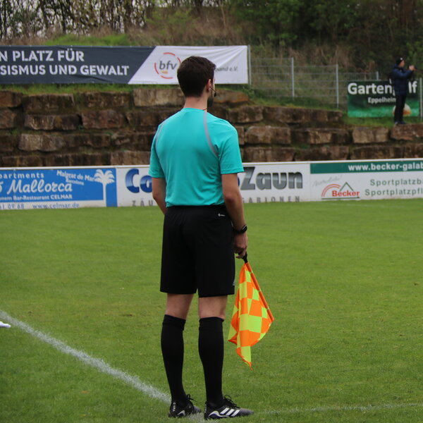 Linienrichter von hinten, er steht am Spielfeldrand und hält eine Fahne in der Hand