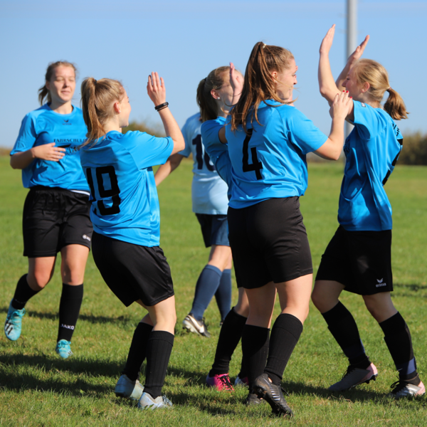 Junge Fußballspielerinnen in blauen Trikots, die jubeln. Sie klatschen sich gegenseitig ab und lächeln.